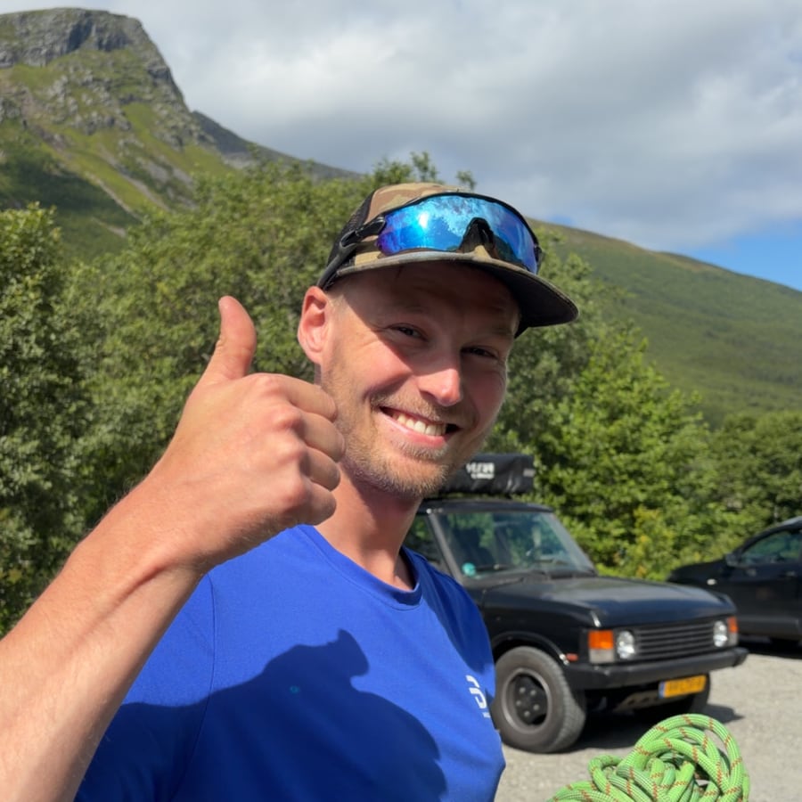 Håvard Hasund utendørs med klatretau, foran fjell og blå himmel